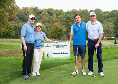 Sponsors of fundraiser golf game posing by signage