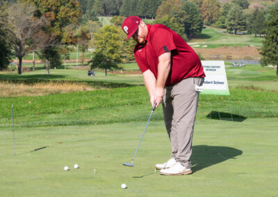 Man in red shirt striking ball on golf course for fundraiser game